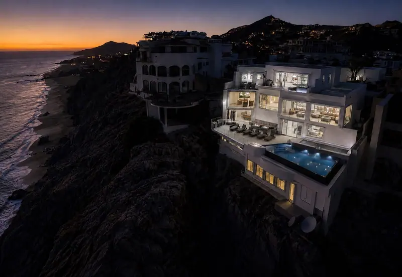 Night aerial of Villa Lands End glowing on the cliff with lit infinity pool